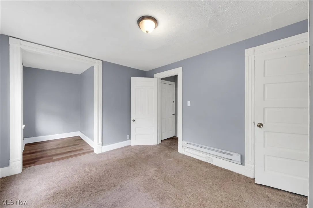 Unfurnished bedroom featuring carpet floors, baseboards, and a baseboard heating unit