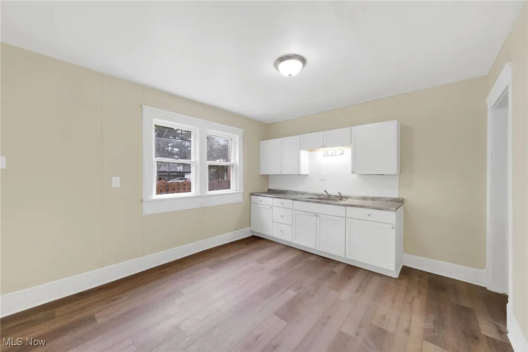 Kitchen with light wood-style floors, a sink, white cabinets, and baseboards