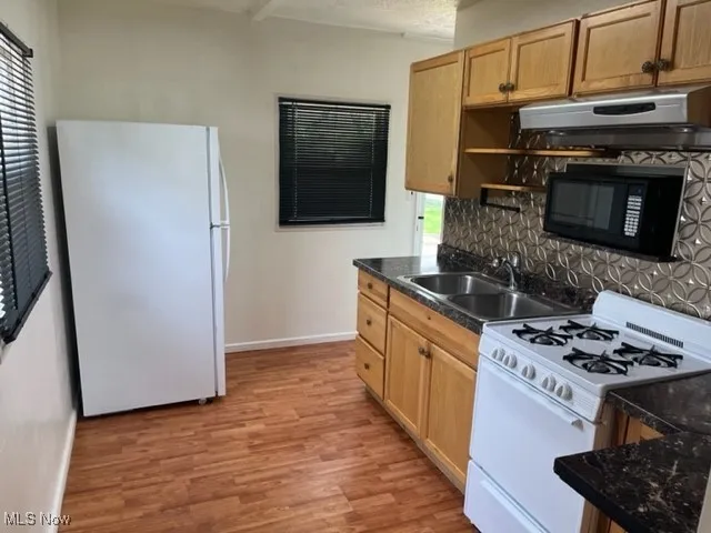 Kitchen featuring white appliances, ventilation hood, a sink, decorative backsplash, and baseboards