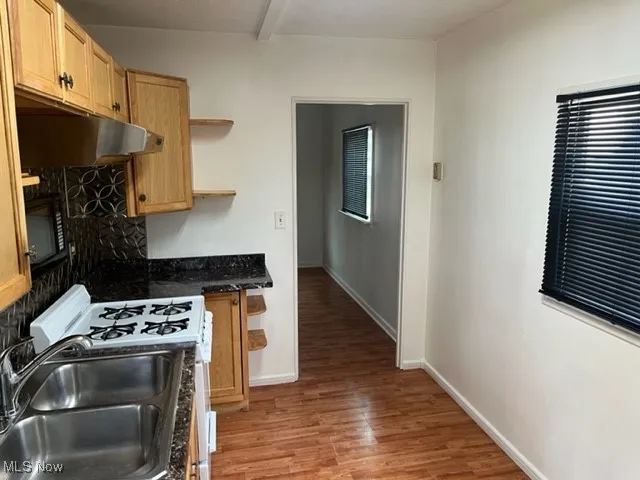 Kitchen with under cabinet range hood, a sink, light wood-type flooring, open shelves, and white gas range