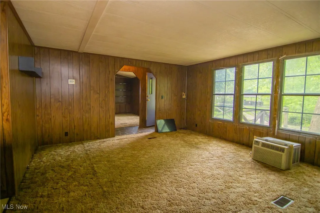 Unfurnished room with a wall mounted AC, arched walkways, wooden walls, and carpet flooring
