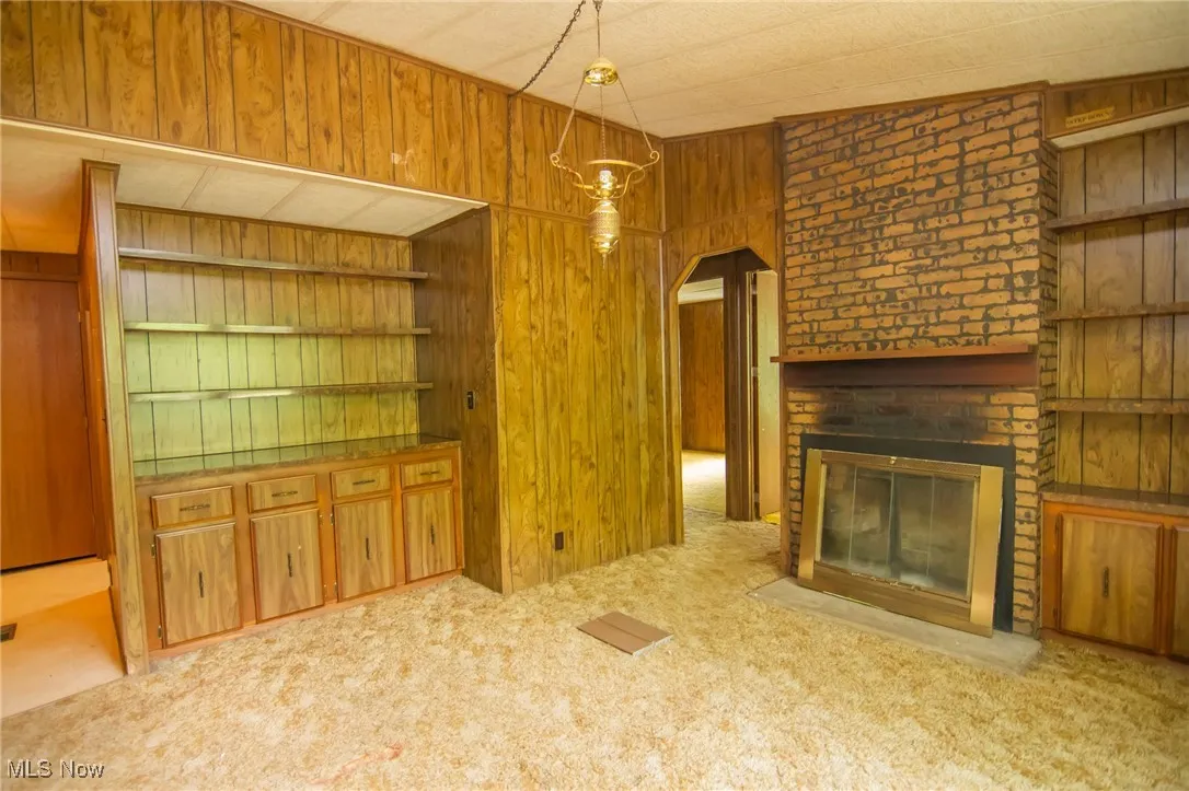 Unfurnished living room with wooden walls, carpet floors, a brick fireplace, and arched walkways
