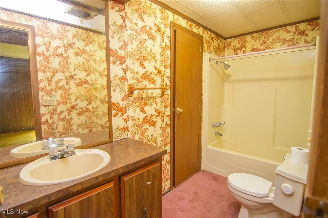 Full bathroom featuring wallpapered walls, toilet, vanity, and washtub / shower combination
