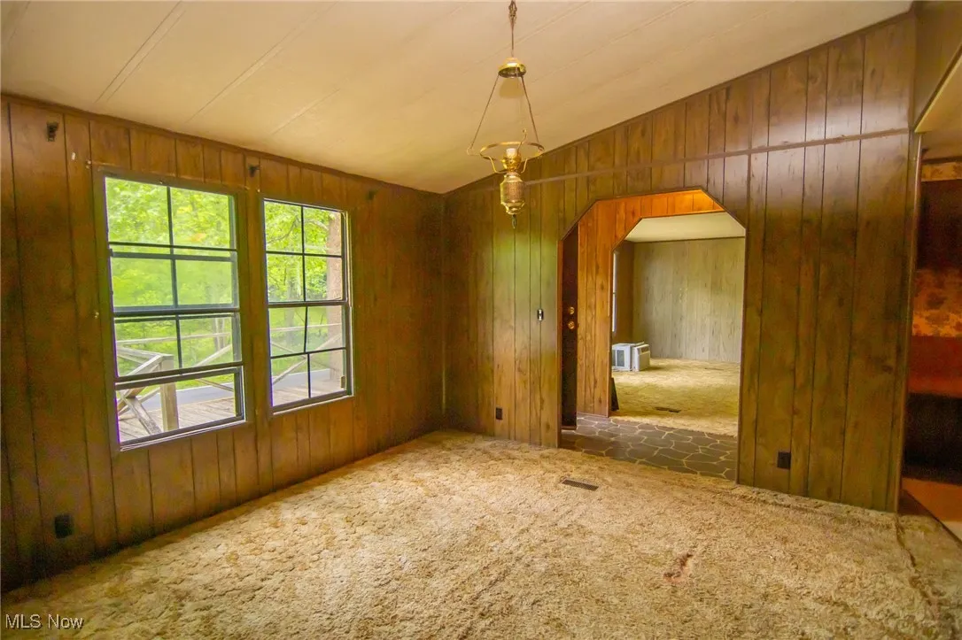 Unfurnished dining area with arched walkways, carpet, wooden walls, and lofted ceiling