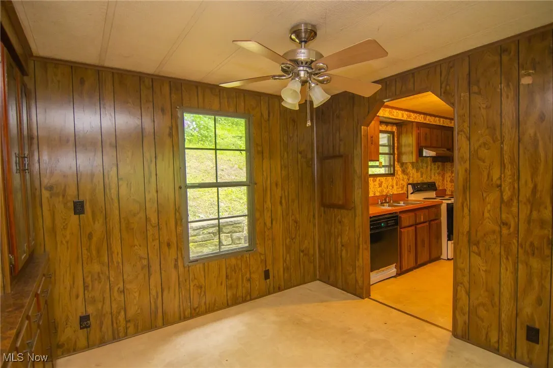 Unfurnished dining area with wood walls, a sink, ceiling fan, arched walkways, and light floors