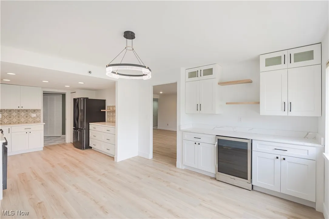 Kitchen featuring beverage cooler, freestanding refrigerator, open shelves, decorative backsplash, and white cabinets