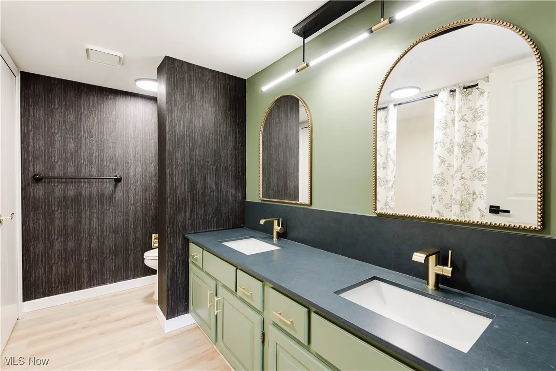 Bathroom with double vanity, toilet, and wood finished floors