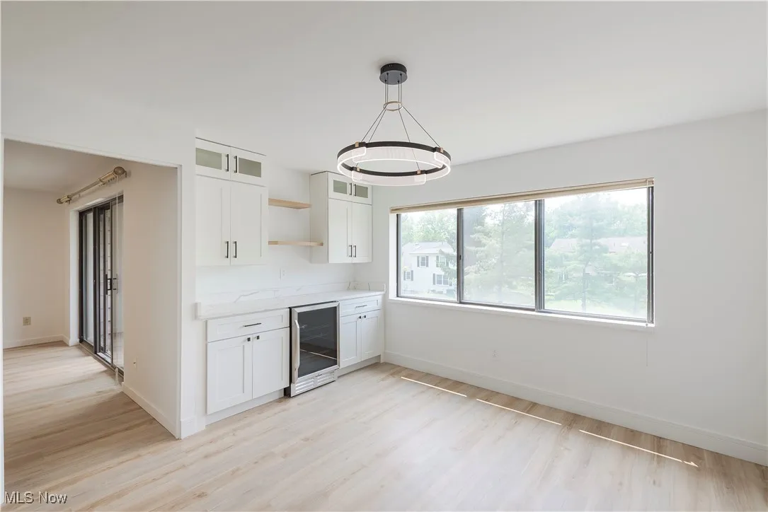 Kitchen featuring beverage cooler, light wood-type flooring, open shelves, a chandelier, and baseboards