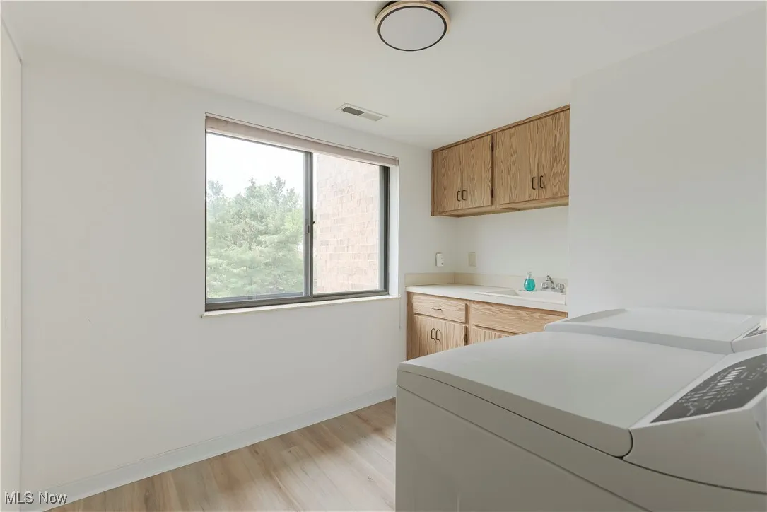 Laundry area with cabinet space, light wood-style flooring, baseboards, and washing machine and dryer