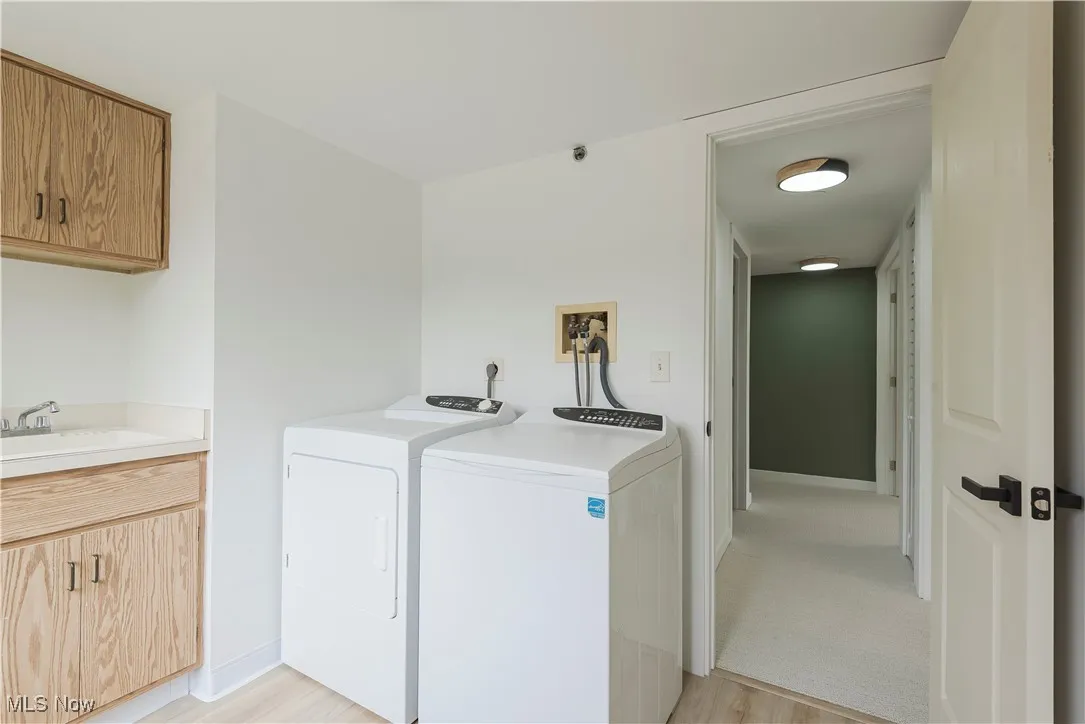 Laundry room with separate washer and dryer, light wood-style flooring, cabinet space, and baseboards