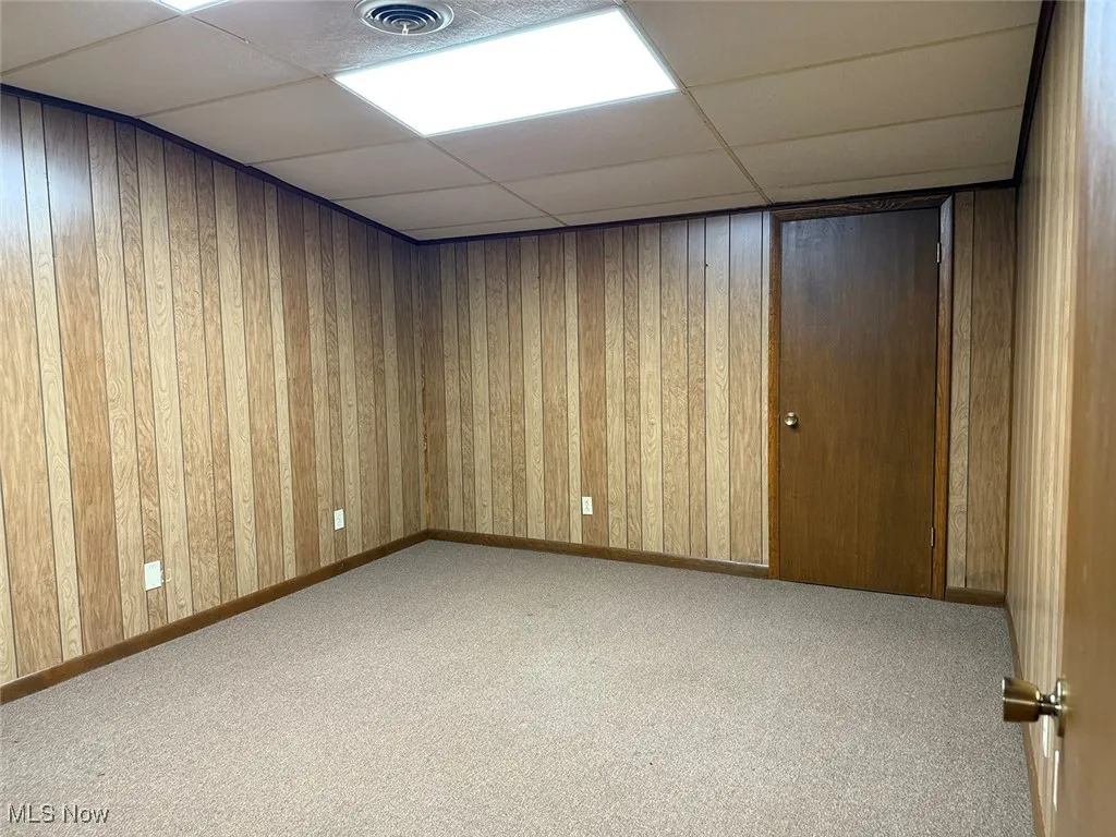 Unfurnished room with a drop ceiling, carpet flooring, and wooden walls