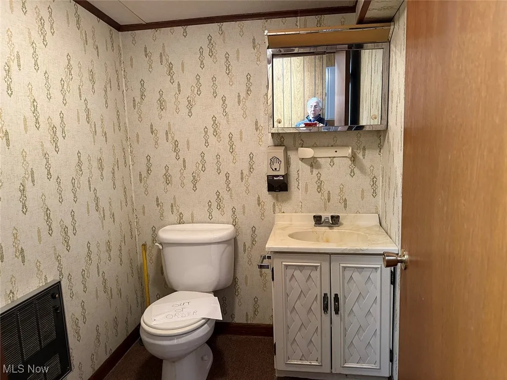 Bathroom with toilet, vanity, heating unit, baseboards, and wallpapered walls