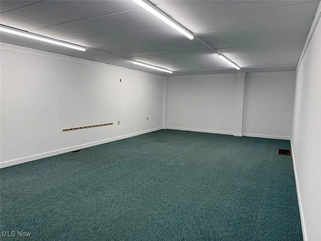 Spare room featuring dark colored carpet and baseboards