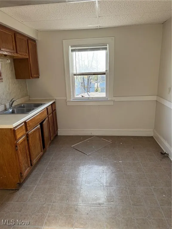 Kitchen with a sink, brown cabinetry, light countertops, and baseboards