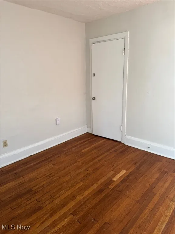 Unfurnished room featuring dark wood-style floors, baseboards, and a textured ceiling