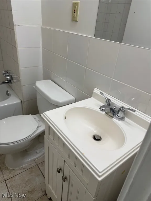 Bathroom featuring tile walls, vanity, toilet, and tile patterned flooring