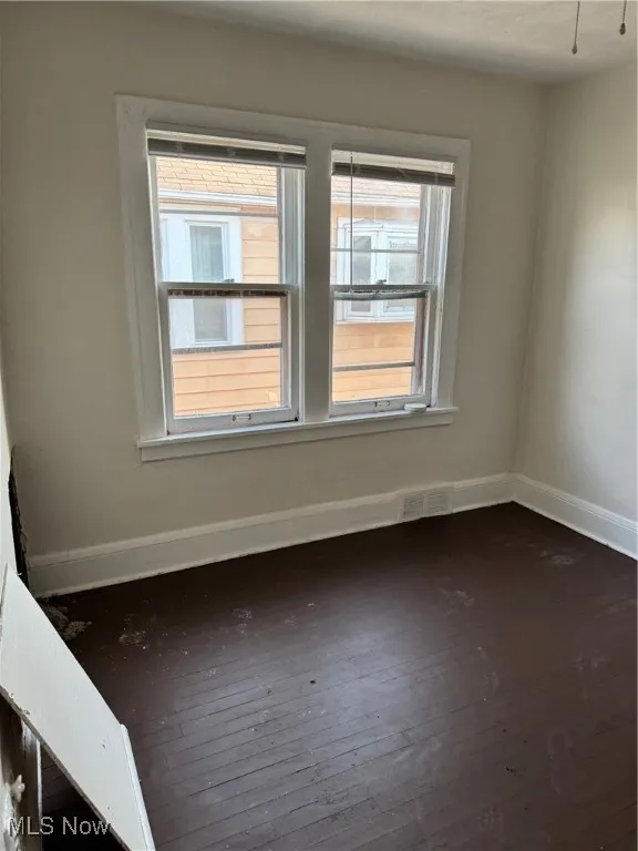 Unfurnished room featuring baseboards and dark wood-type flooring