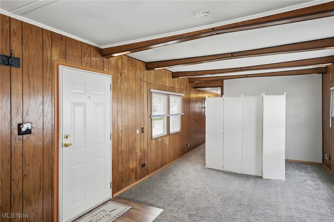 Entryway featuring wooden walls, carpet, beam ceiling, and baseboards