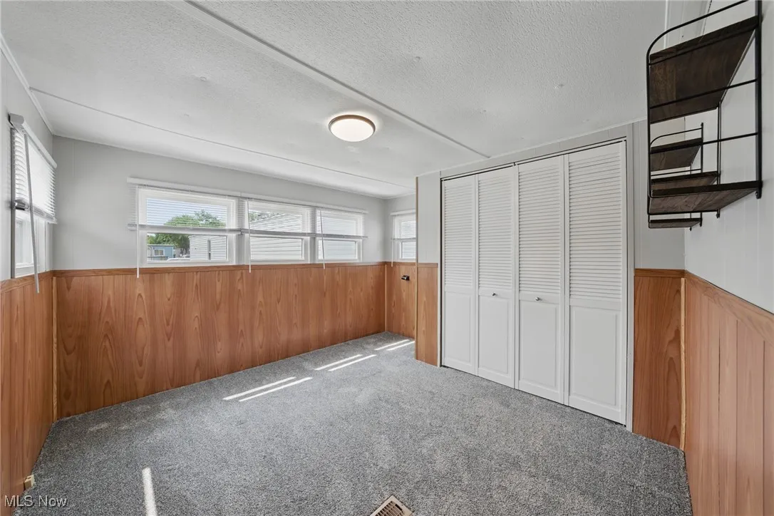 Unfurnished bedroom with wood walls, wainscoting, multiple windows, a closet, and a textured ceiling