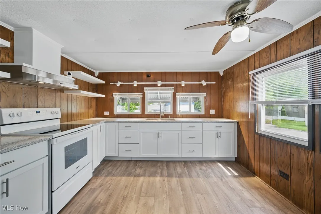 Kitchen with white range with electric stovetop, open shelves, wall chimney exhaust hood, wood walls, and light wood-style floors