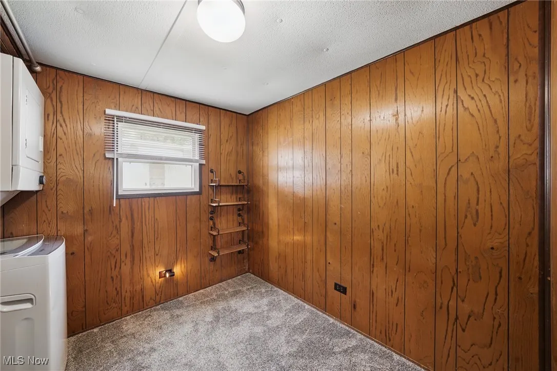 Carpeted spare room featuring wood walls, stacked washer / dryer, and a textured ceiling