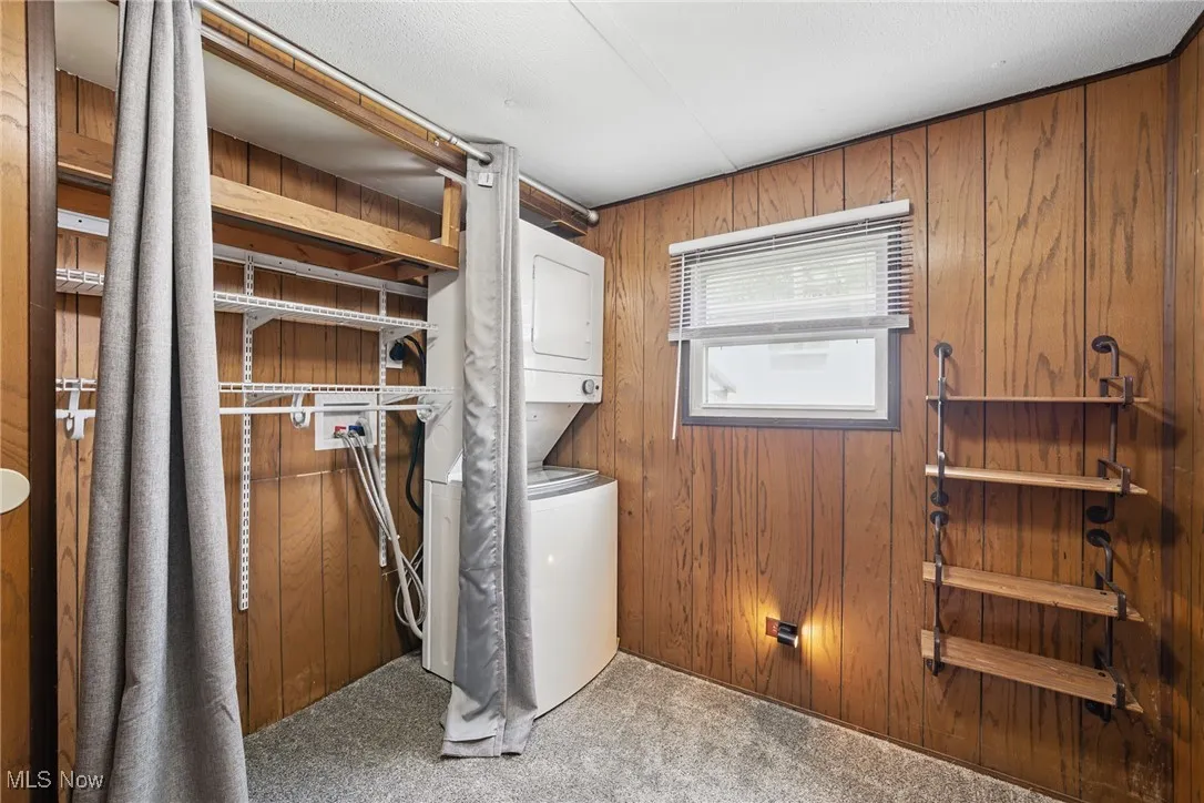 Laundry room with estacked washer and dryer, carpet floors, and wooden walls
