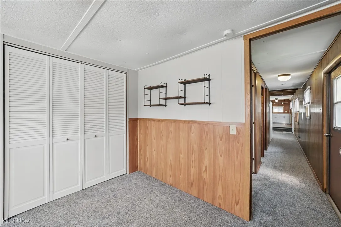Hallway featuring carpet, wood walls, a textured ceiling, and a wainscoted wall
