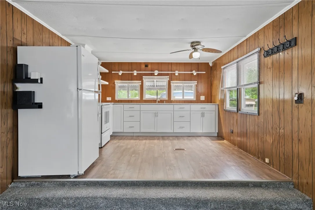 Kitchen featuring white appliances, white cabinets, wood walls, light wood-type flooring, and a ceiling fan