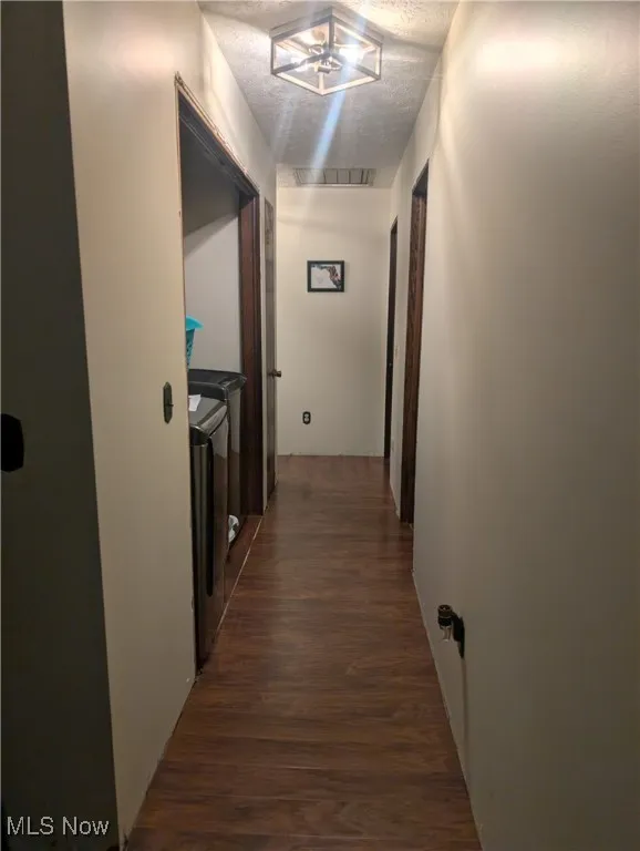 Corridor with washing machine and clothes dryer, dark wood finished floors, and a textured ceiling