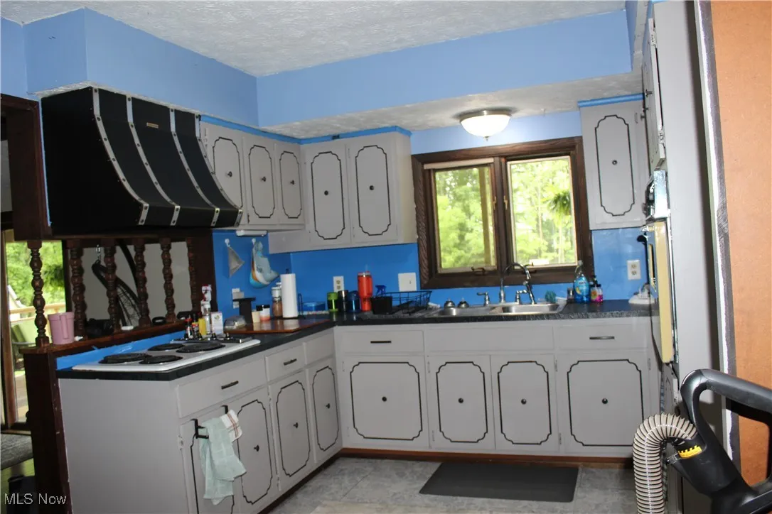 Kitchen with a sink, ventilation hood, dark countertops, white electric stovetop, and a textured ceiling