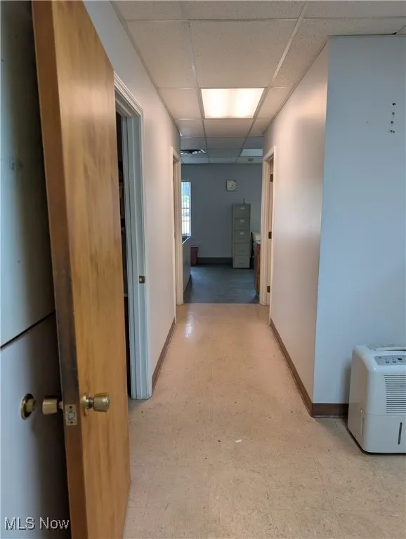 Hall with a drop ceiling, light floors, and baseboards