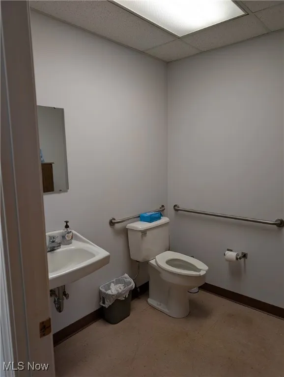 Half bathroom with toilet, tile patterned floors, baseboards, a drop ceiling, and a sink