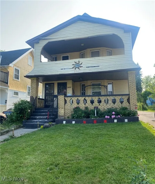 View of front facade featuring covered porch, a front lawn, and brick siding