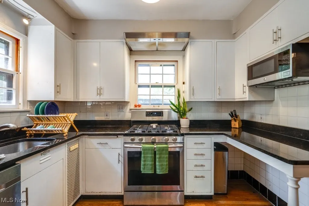 Kitchen with appliances with stainless steel finishes, a sink, white cabinets, and wood finished floors