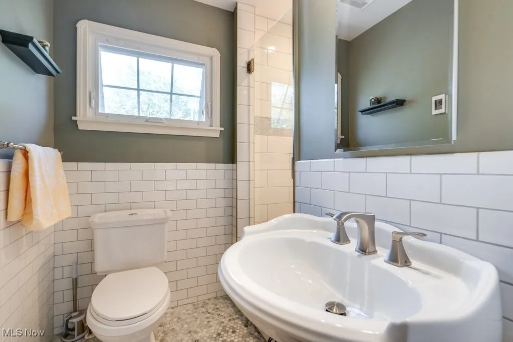 Bathroom with tile walls, a sink, toilet, and wainscoting