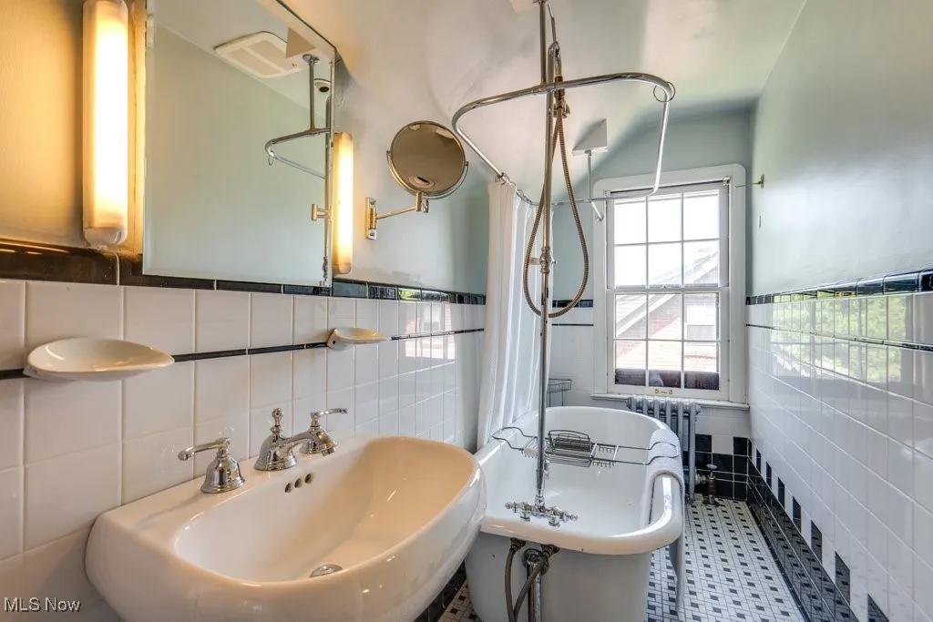 Bathroom featuring tile walls, a sink, a freestanding bath, radiator, and curtained shower