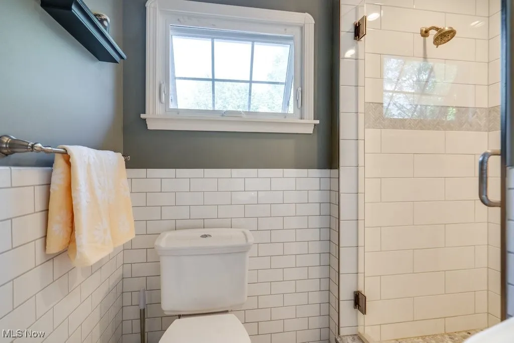 Bathroom with a stall shower, tile walls, toilet, and wainscoting