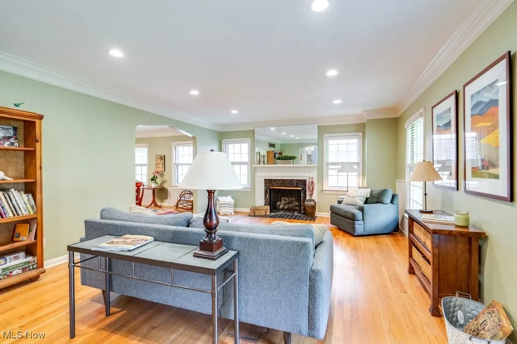 Living room with arched walkways, light wood-style floors, ornamental molding, recessed lighting, and a fireplace