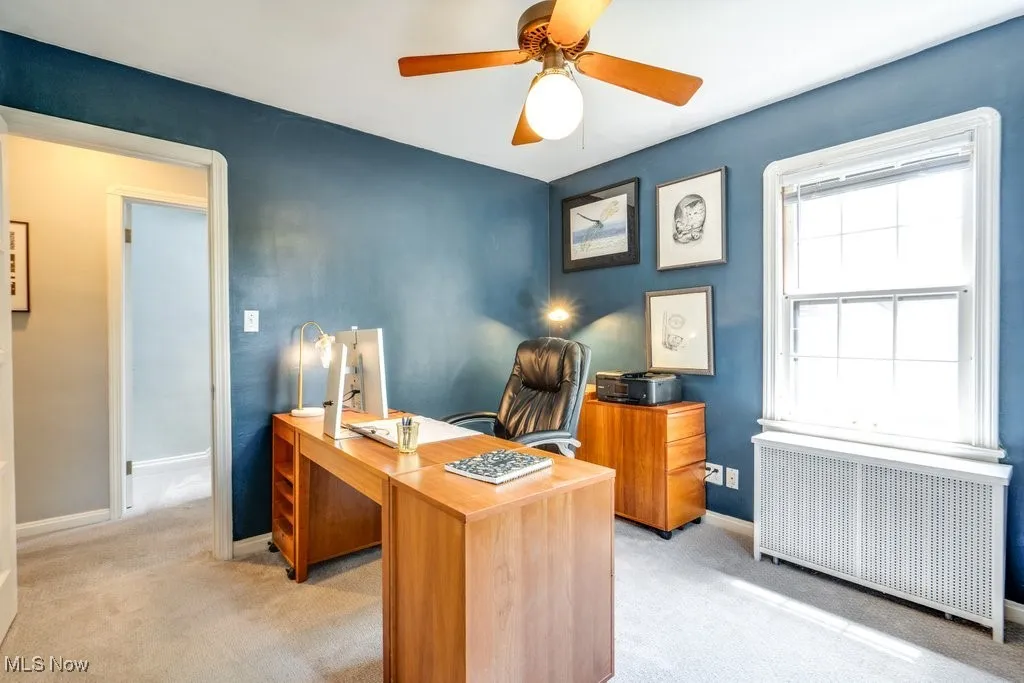 Office area with radiator, light carpet, baseboards, and a ceiling fan