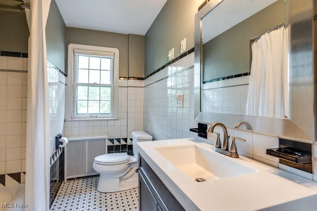 Bathroom with tile walls, radiator heating unit, toilet, a shower with curtain, and vanity