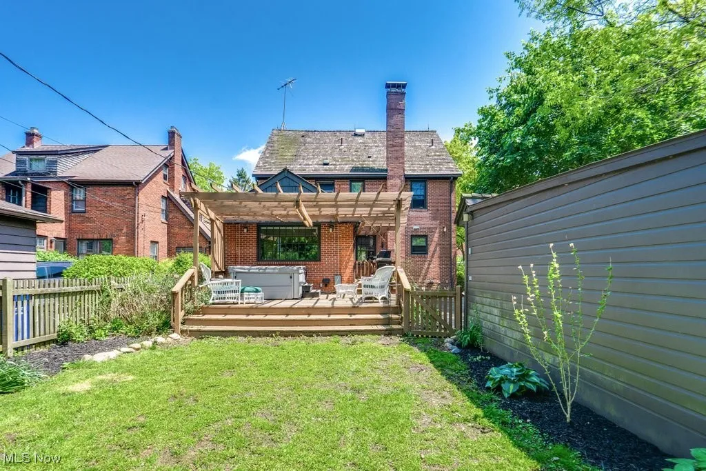 Back of property with a pergola, a deck, brick siding, and a chimney