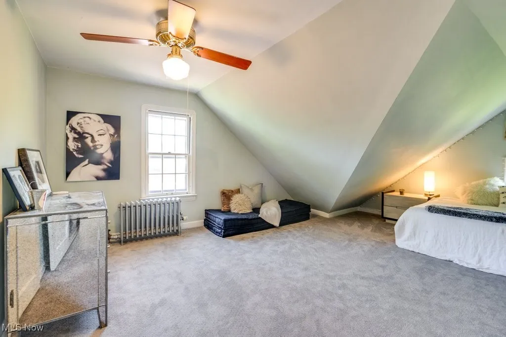 Carpeted bedroom with radiator, vaulted ceiling, baseboards, and a ceiling fan
