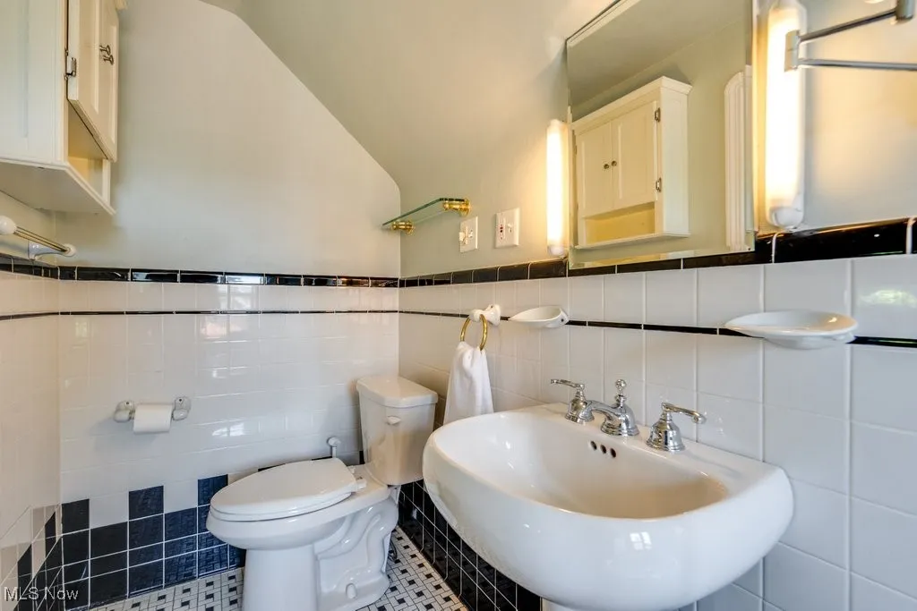 Bathroom featuring tile walls, a sink, toilet, a wainscoted wall, and tile patterned flooring