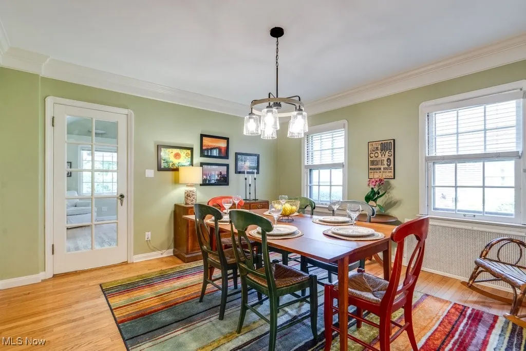 Dining room with wood finished floors, ornamental molding, a chandelier, baseboards, and radiator heating unit