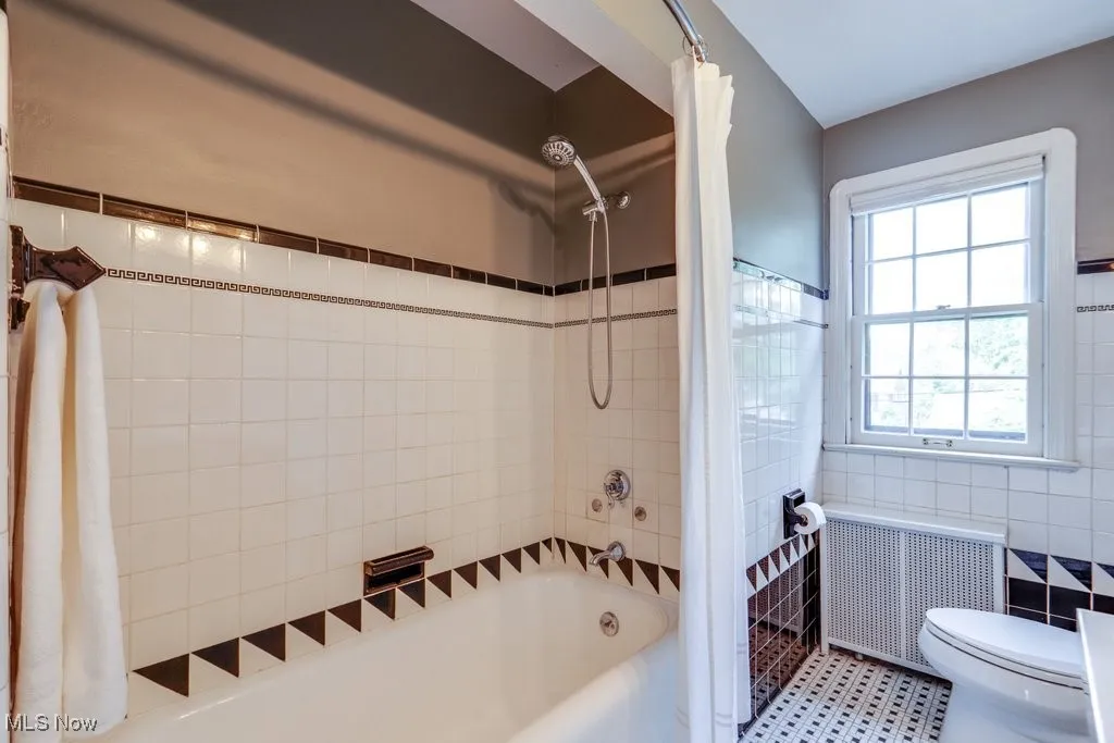 Full bathroom with radiator, tile walls, shower / bath combo with shower curtain, and toilet