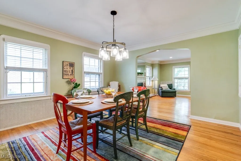Dining room with arched walkways, light wood finished floors, ornamental molding, a chandelier, and baseboards