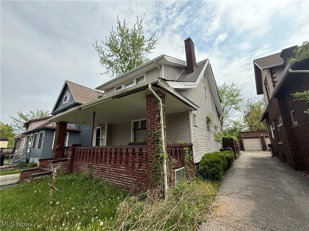 View of side of property featuring a chimney, an outbuilding, covered porch, a detached garage, and driveway