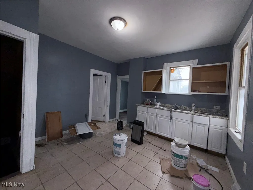 Kitchen featuring open shelves, light stone countertops, white cabinetry, light tile patterned flooring, and baseboards