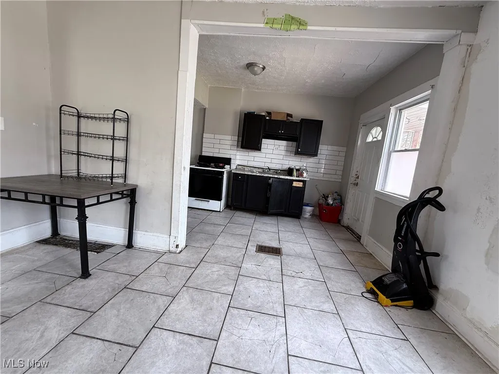 Kitchen featuring electric stove, dark cabinetry, tasteful backsplash, a sink, and baseboards