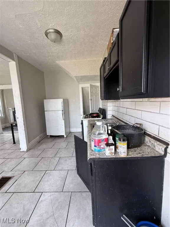 Kitchen featuring refrigerator, tasteful backsplash, dark cabinetry, a textured ceiling, and baseboards